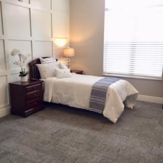 A cozy bedroom with a single bed, nightstand, and a lamp by the window.