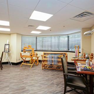 An art studio with looms and crafting supplies, featuring large windows and spacious seating.