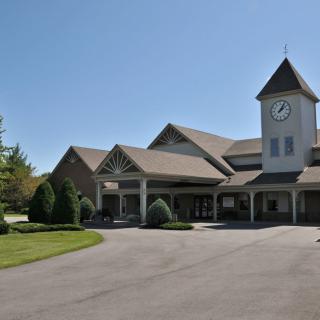 A large clock tower building with a spacious driveway and surrounding greenery.