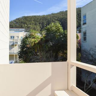 A scenic balcony view featuring lush greenery and adjacent buildings under a clear blue sky.
