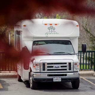 A white shuttle bus parked in a lot, partially obscured by tree leaves.