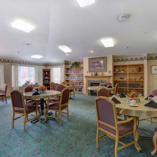A cozy dining area with round tables, chairs, a fireplace, and bookshelves.