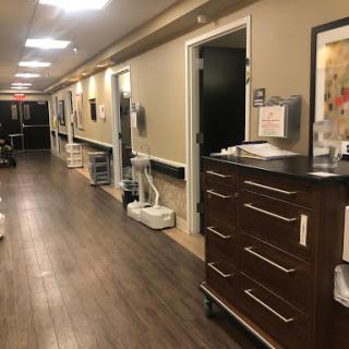 A view down a well-lit hallway in a medical facility, showcasing doors and furniture typical of a hospital setting.