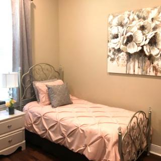 A cozy and elegantly designed bedroom featuring a single bed with pink bedding, complemented by floral wall art and a stylish nightstand.