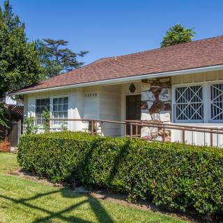 A charming single-story house with a well-maintained garden and hedges under a clear blue sky.