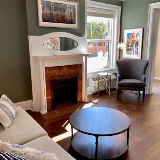 A cozy living room with a fireplace, sofa, armchair, and coffee table, featuring elegant decor and artwork.