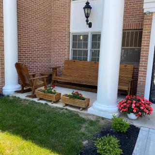 A cozy outdoor porch area featuring a wooden bench and chairs, surrounded by colorful flower arrangements and sturdy columns.