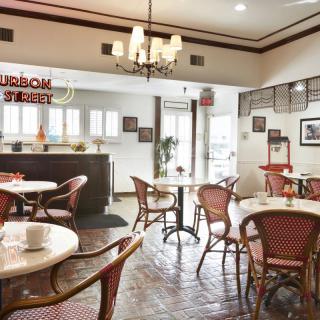 A cozy restaurant interior with elegantly arranged tables and chairs, featuring a chandelier and warm decor.