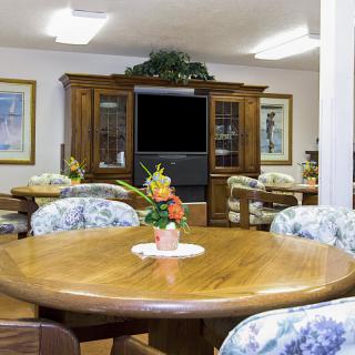A cozy dining area with a wooden table, floral chairs, and a television in a wooden cabinet.