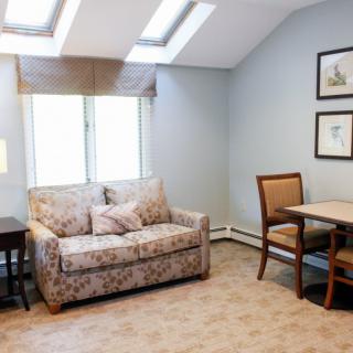 A cozy living room with a floral sofa and armchair, lit by natural light through the window and skylights.