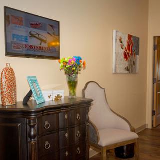 A cozy interior space featuring a dark wooden dresser, a decorative vase with vibrant flowers, and stylish artwork on the walls.