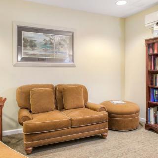 A cozy living room with a brown sofa, bookshelf, and artwork on the wall.