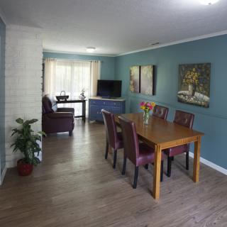 A cozy dining and living area with a wooden table, chairs, artwork on the walls, and a TV.