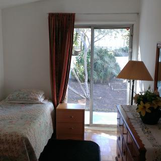 A cozy bedroom with a single bed, dresser, and a large window overlooking the garden.