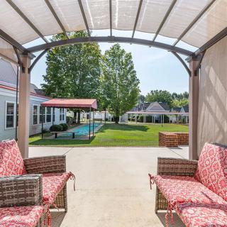 A cozy patio with rattan furniture and red cushions under a covered area, overlooking a spacious backyard.
