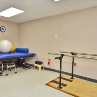 A clean rehabilitation room equipped with exercise balls, a therapy table, and parallel bars.