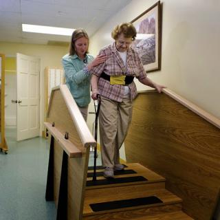 A caregiver assists an elderly individual as they navigate stairs, highlighting the importance of support in rehabilitation.