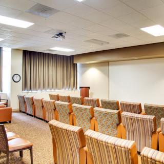 An empty conference room with a podium and arranged seating facing a projector screen.