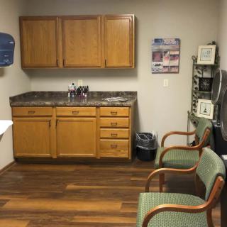 An office waiting room with wooden cabinets, a sink, and chairs arranged on a wooden floor.