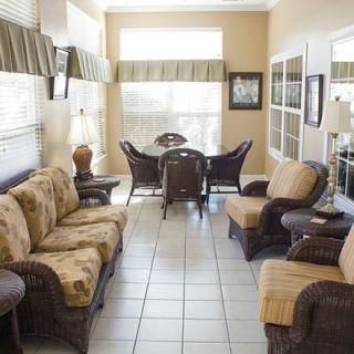 A cozy living room featuring wicker sofas and chairs, with a dining table set near large windows.