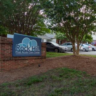 A sign for Rock Hill on a brick base, surrounded by trees and parked cars.