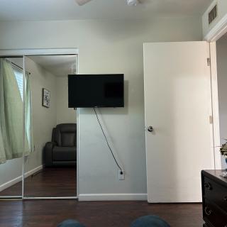 A room interior with a wall-mounted television, a door, and mirrored closet doors.
