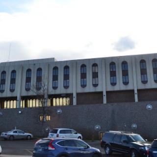 A view of a modern architectural building with a cloudy sky in the background, surrounded by parked vehicles.