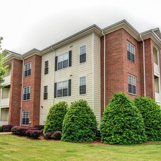 A residential apartment building with brick and siding exterior, surrounded by neatly trimmed bushes and greenery.