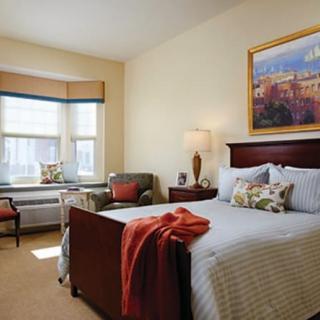A cozy bedroom with a neatly made bed, armchair, and window view.