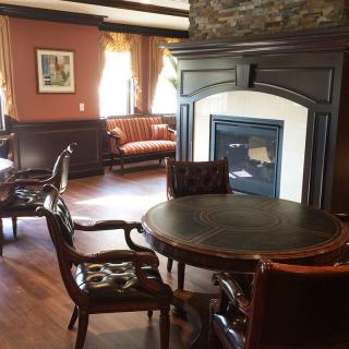 A cozy room with traditional decor features a central fireplace, surrounded by dark wood furniture and elegant window curtains.