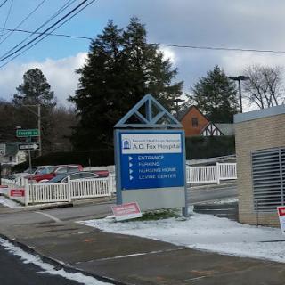 A view of a building entrance with a sign, surrounded by snow and trees on a winter day.