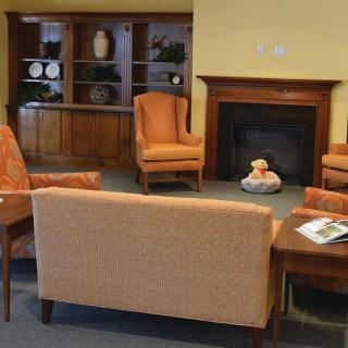 A cozy living room setup featuring a sofa, armchairs, and a fireplace with a decorative shelf in the background.