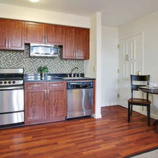 A modern kitchen with stainless steel appliances, wood cabinetry, and a small dining table in an open layout.