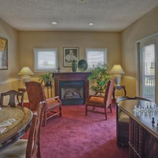 A cozy living room with a fireplace, chairs, and a chessboard on a table.