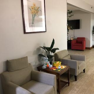 A cozy waiting area featuring two chairs, a small table with refreshments, and a potted plant, enhanced by a floral artwork on the wall.