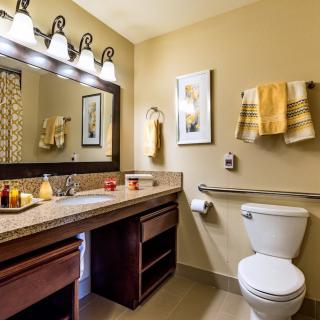 A well-lit bathroom with a large mirror, sink, and neatly arranged towels.