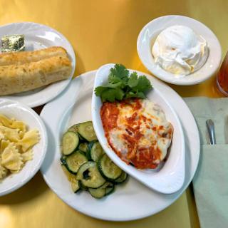 A delicious dinner plate featuring pasta, sauted cucumbers, a cheese-topped dish, and a side of dessert.