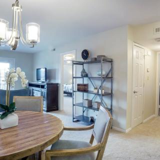 A modern dining and living area with a round wooden table, stylish chairs, and a decorative chandelier in a neutral color scheme.