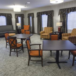 A cozy living room featuring several seating areas with armchairs and tables, complemented by lamps and curtains.