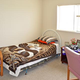 A small, cozy bedroom with a single bed and a chair next to a window.