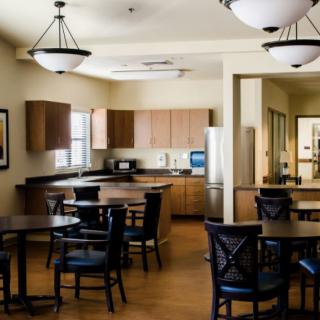 A modern kitchen and dining area featuring wooden cabinets, a stainless steel fridge, and multiple tables with chairs.
