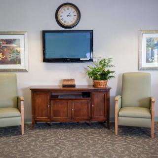 A well-organized waiting room with two chairs, a television, and a clock on the wall.