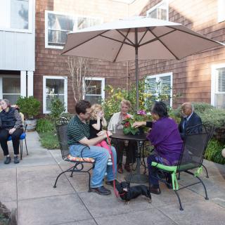 A group of people socializing on a patio under an umbrella.