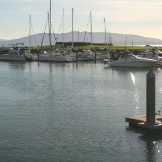 A scenic view of boats and yachts docked in a marina with mountains in the background at sunset.