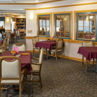 A well-lit dining area with tables and chairs, featuring maroon tablecloths and elegant decor.