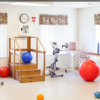 A rehabilitation room equipped with exercise balls, a stationary bike, and steps for physical therapy exercises.