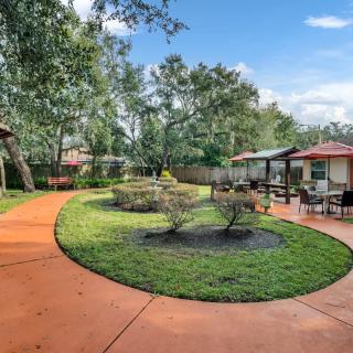A landscaped garden with a circular pathway, surrounded by trees and shrubs, adjacent to a house with a patio.