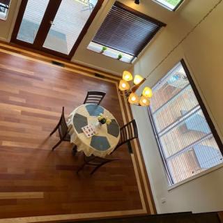 A cozy dining area with wooden flooring, featuring a round table and chairs, illuminated by a chandelier.