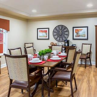 A well-decorated dining room with a wooden table set for six, featuring elegant chairs and a large wall clock.