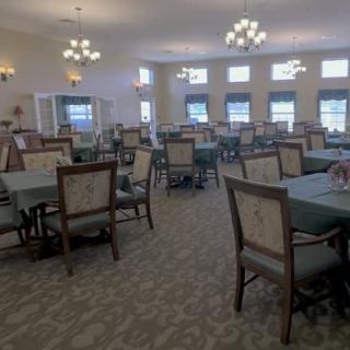 A spacious dining room with multiple tables and chairs, illuminated by chandeliers.